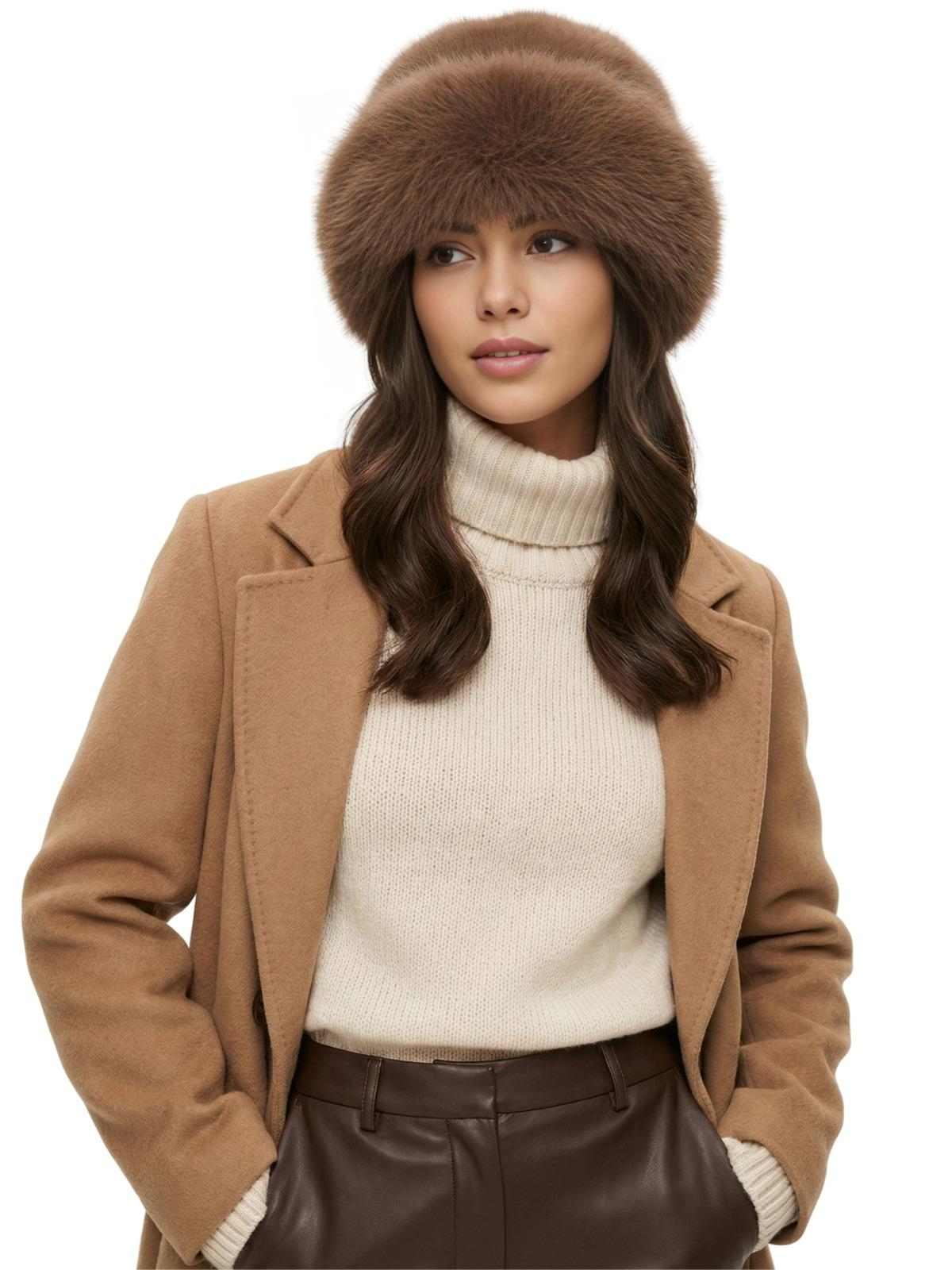 Woman wearing a brown faux fur hat, beige coat, white turtleneck sweater, and brown pants on a white background