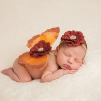 Thumbnail for Newborn baby in a pumpkin costume with flower headbands on a soft surface