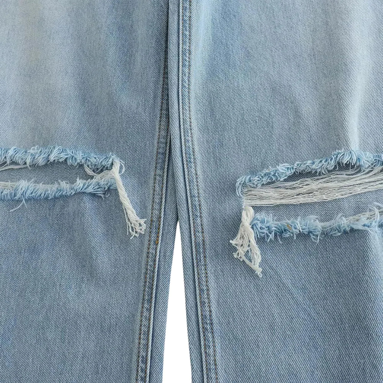 Close-up of a light blue denim jeans with ripped frayed edges on a white background