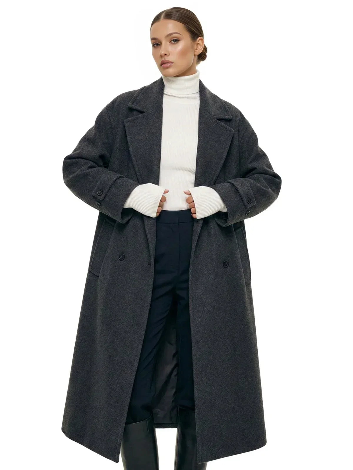 Woman wearing a long dark grey oversized double breasted coat with pockets and turn down collar on a white background.