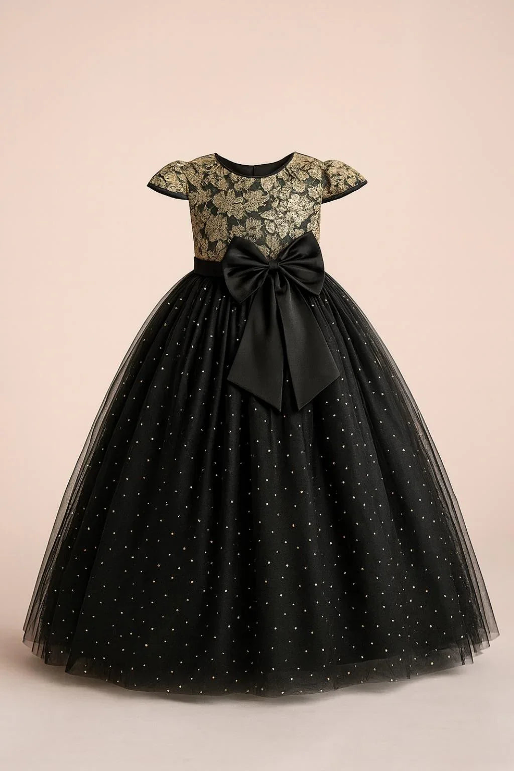 Black dress with gold lace top and bow on a beige background