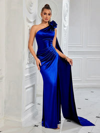 Thumbnail for Woman wearing a blue satin one-shoulder gown with a high slit and floral detail against a white wall.