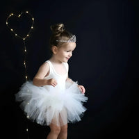 Thumbnail for Young girl in a white sleeveless ballet tutu dress and tiara standing against a dark background