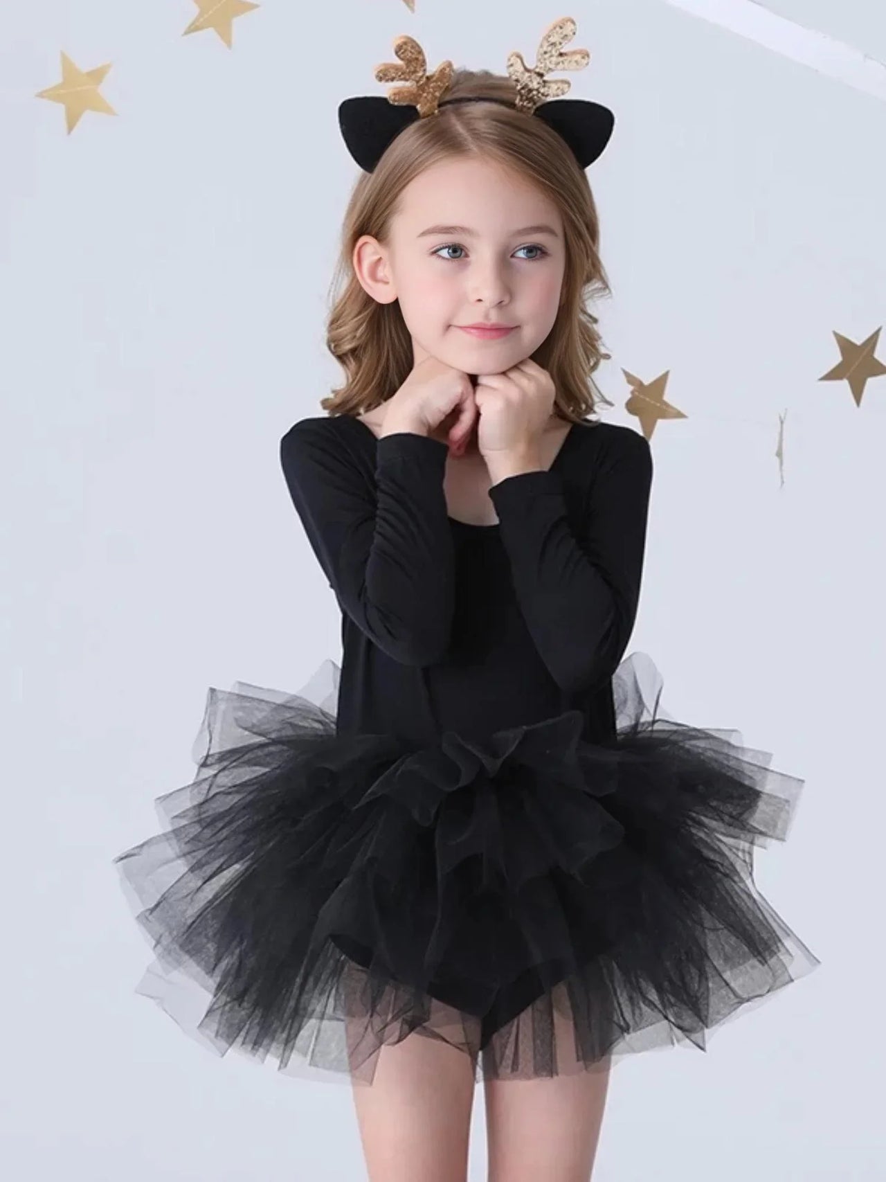 Young girl wearing a black long sleeved ballet tutu dress against a white background with gold stars