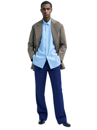 Thumbnail for Man wearing a light blue shirt, dark blue pants, and a brown jacket on a white background