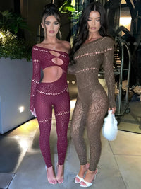 Thumbnail for Two women in sheer outfits standing in an indoor setting with plants and a cart in the background.
