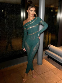 Thumbnail for Woman in a teal, one-shoulder, long-sleeve jumpsuit standing against a dark background.