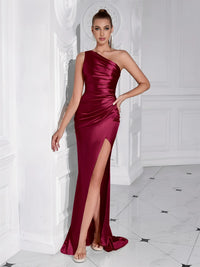 Thumbnail for Woman wearing a burgundy one-shoulder draped maxi dress with a high slit in a white room.