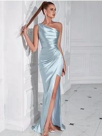 Thumbnail for Woman wearing a sky blue one-shoulder draped maxi dress with a high slit in a white room.