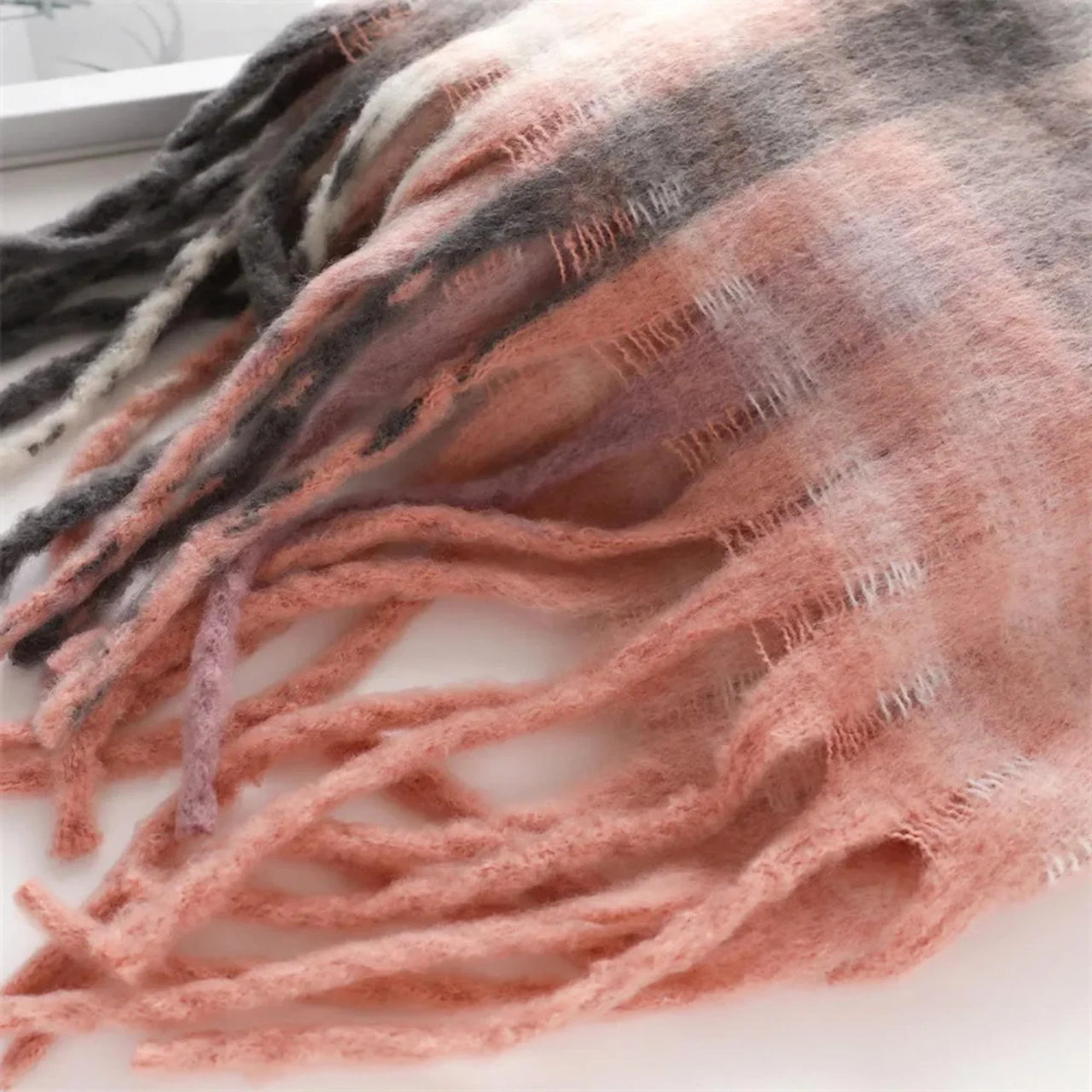 Close-up of a pink and gray striped scarf with tassels on a white background