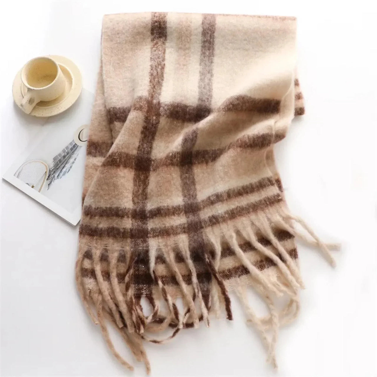 Plaid scarf with fringes on a white surface with a cup and saucer.
