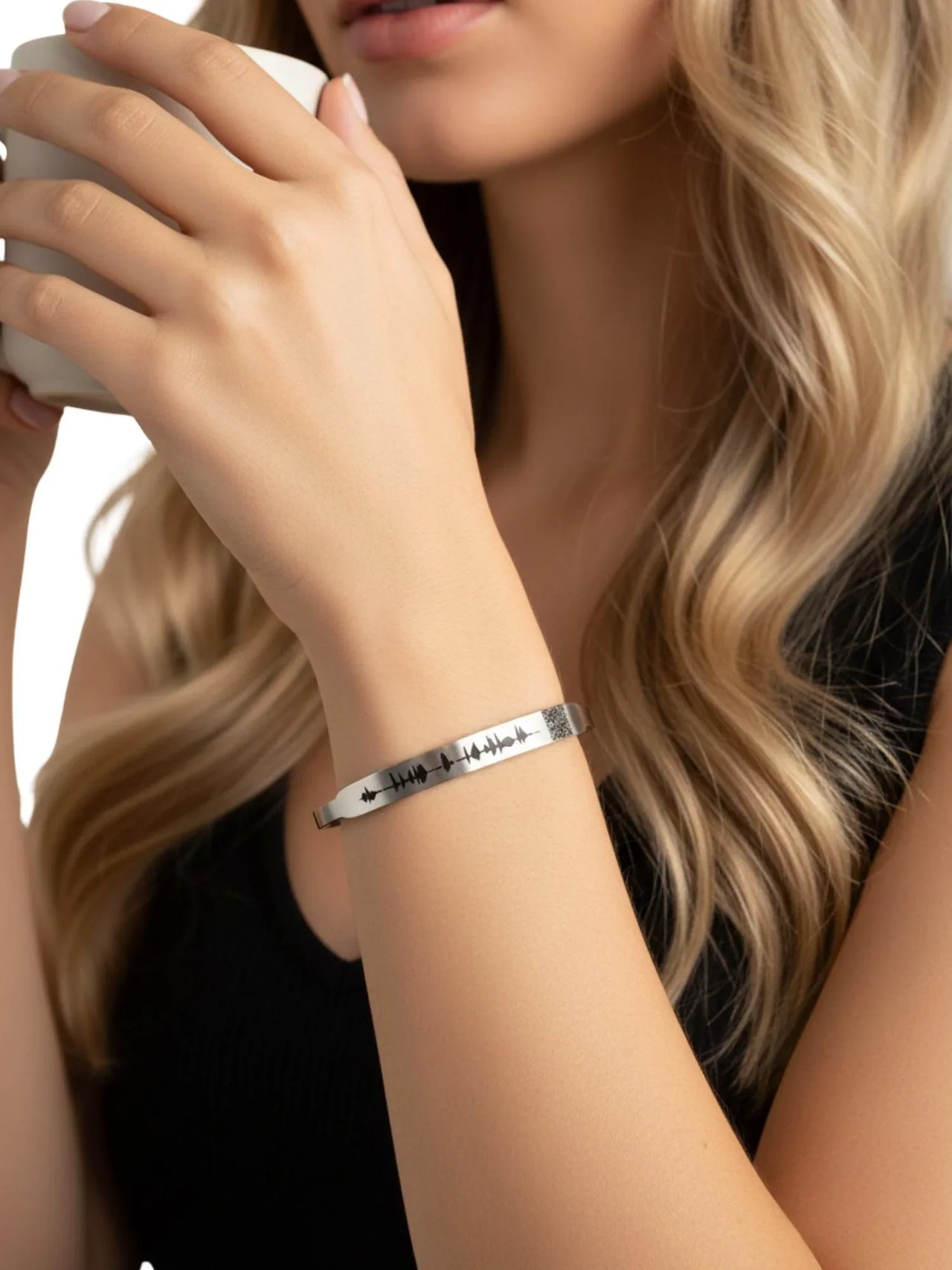 Woman holding a coffee cup wearing a silver voice bracelet with QR code on a white background