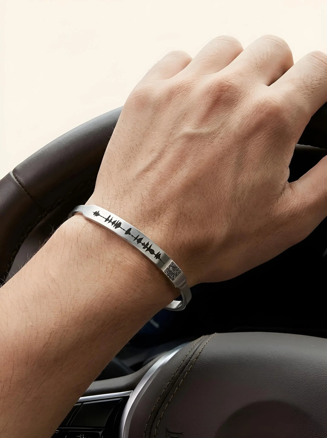 Hand on car steering wheel wearing a silver bracelet with engraved design