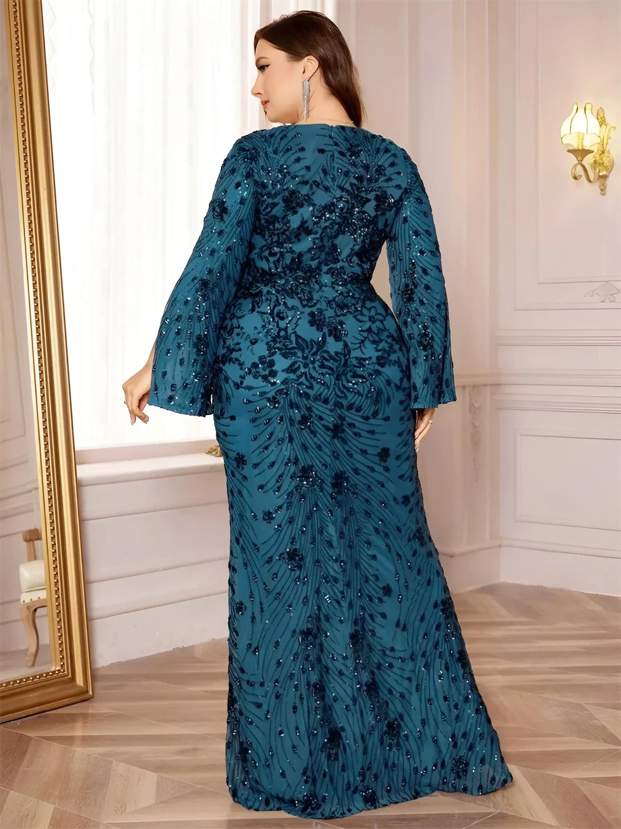 Woman wearing a plus size teal evening gown with floral patterns in an elegant room.