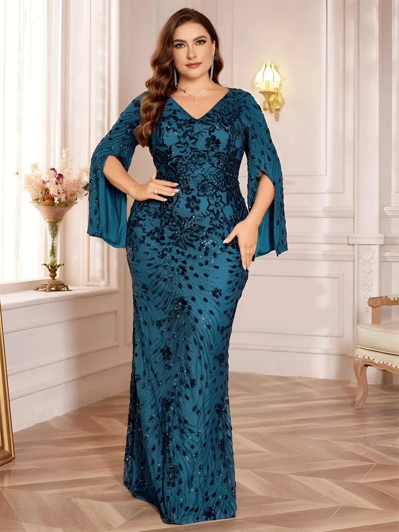 Woman wearing a plus size teal evening gown with floral patterns in an elegant room.