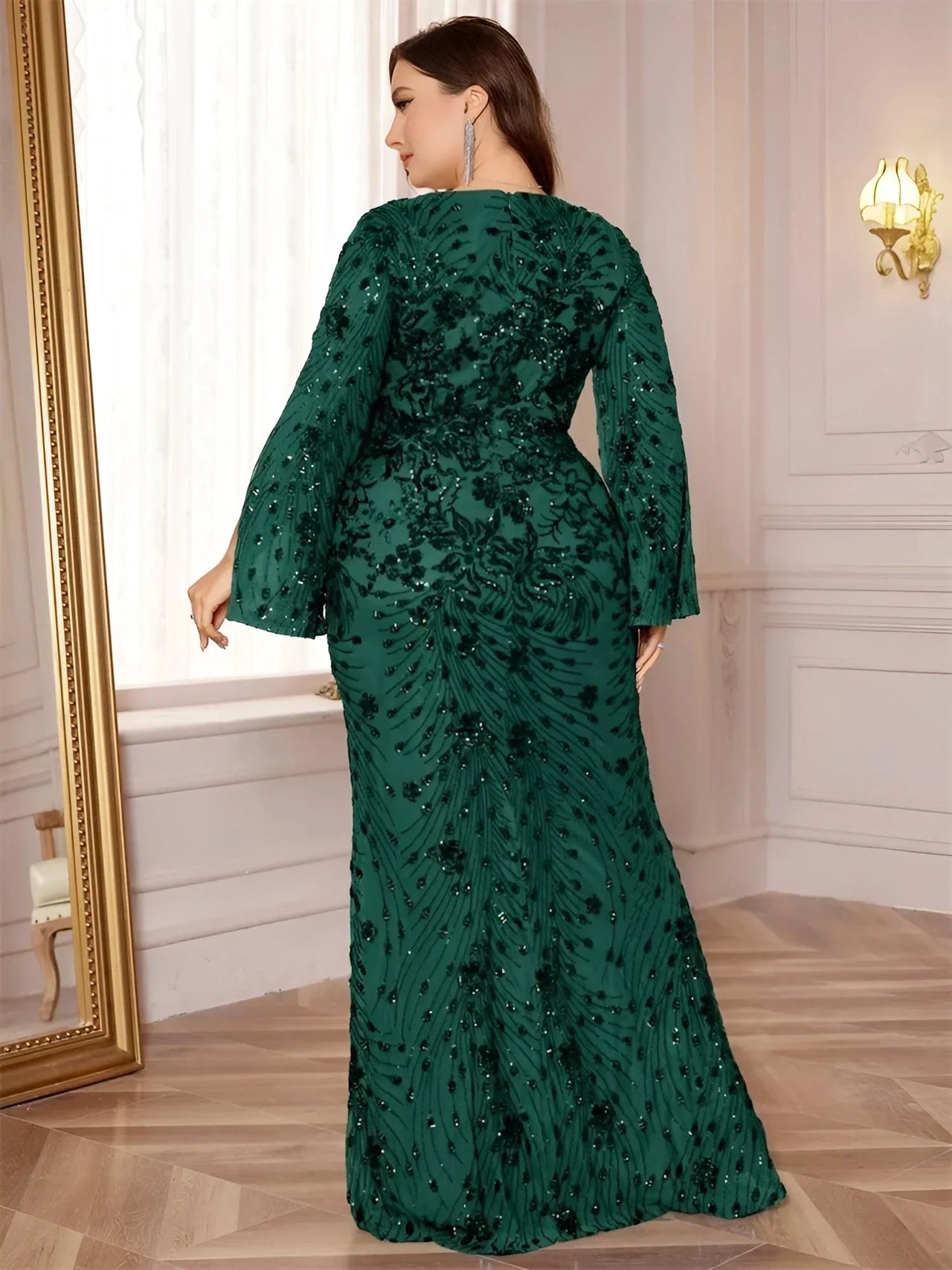 Woman wearing a dark green plus size evening gown with floral patterns in an elegant room.