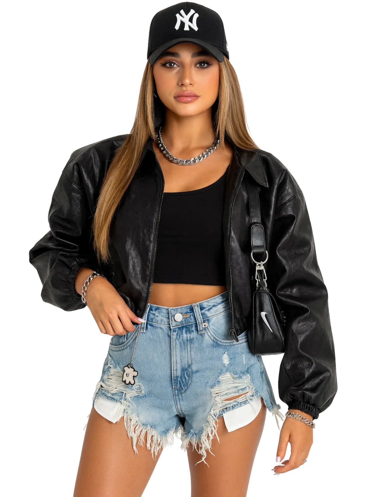 Woman wearing a black leather jacket, black crop top, ripped denim shorts, and a black cap with a white logo on a white background.