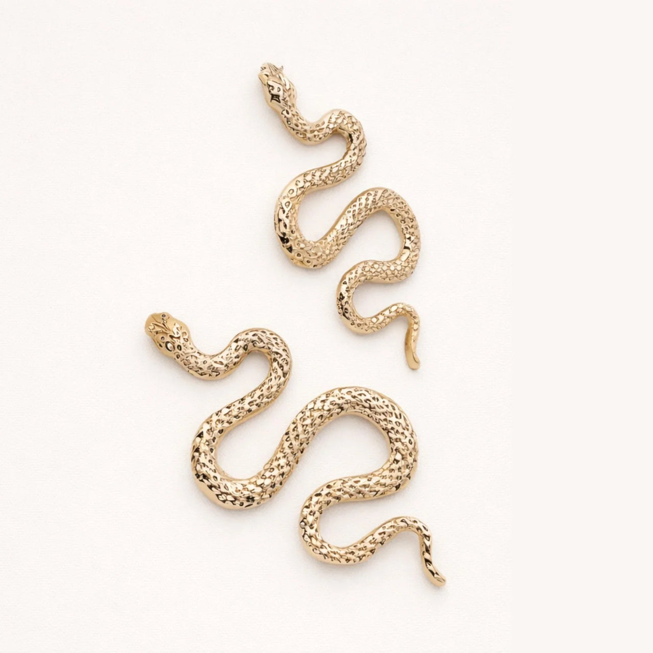Gold snake earrings on a white background