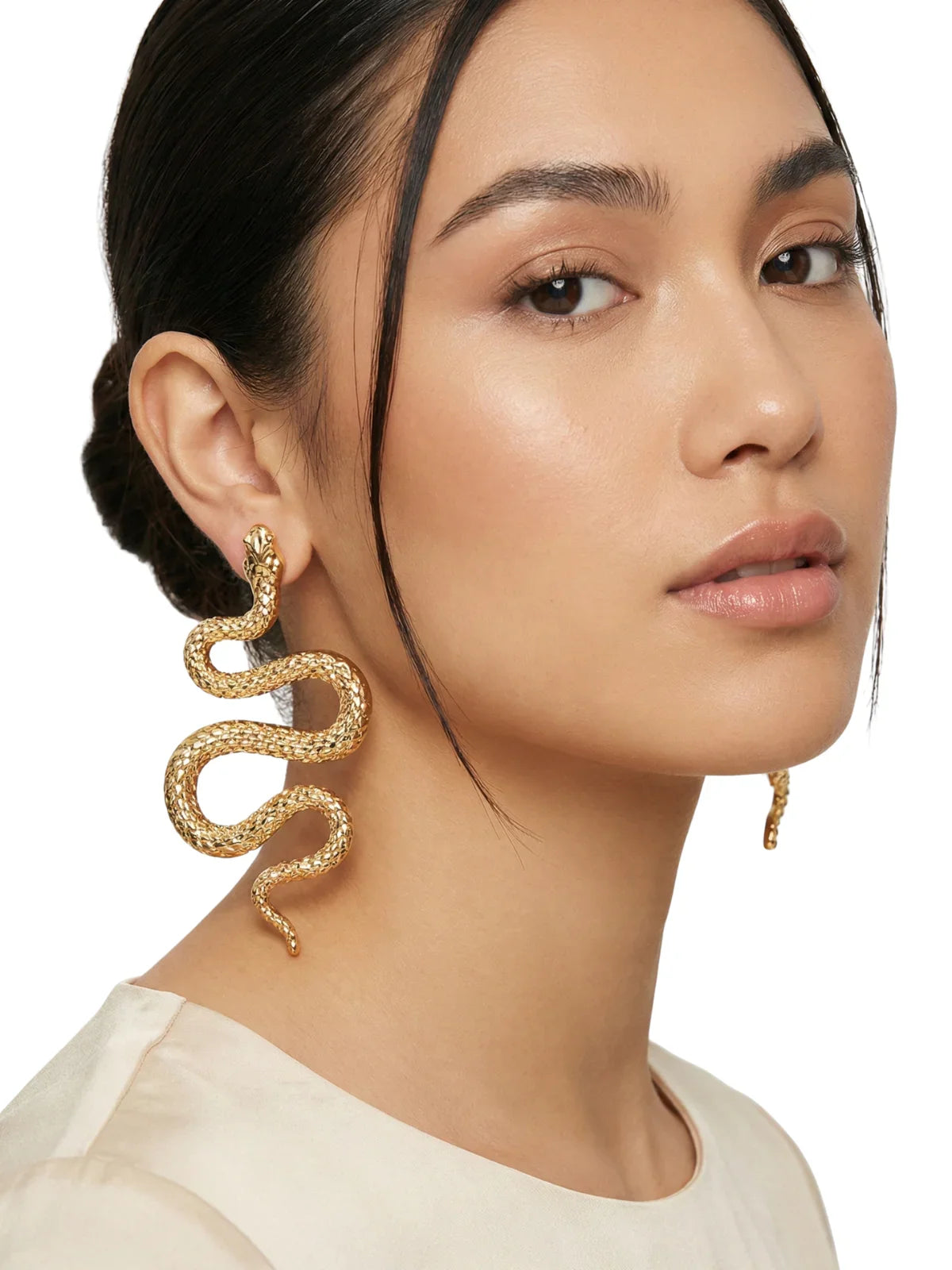 Woman wearing gold snake earrings on a neutral background