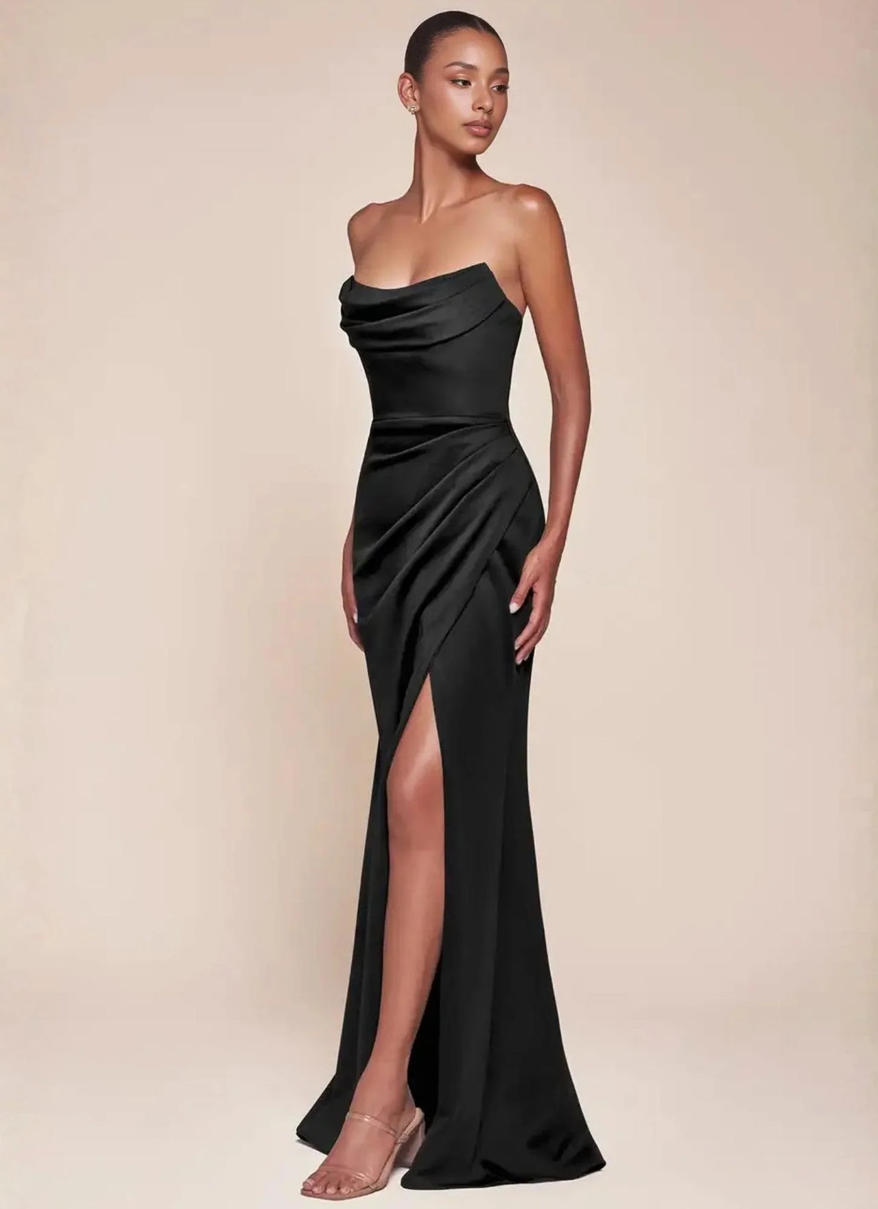 Woman wearing a black strapless evening gown with a high split on a beige background