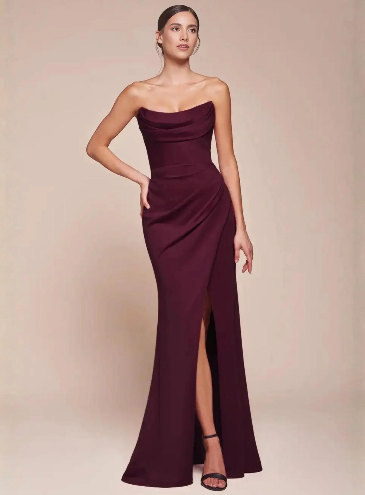 Woman wearing a burgundy strapless evening gown with a high split on a beige background