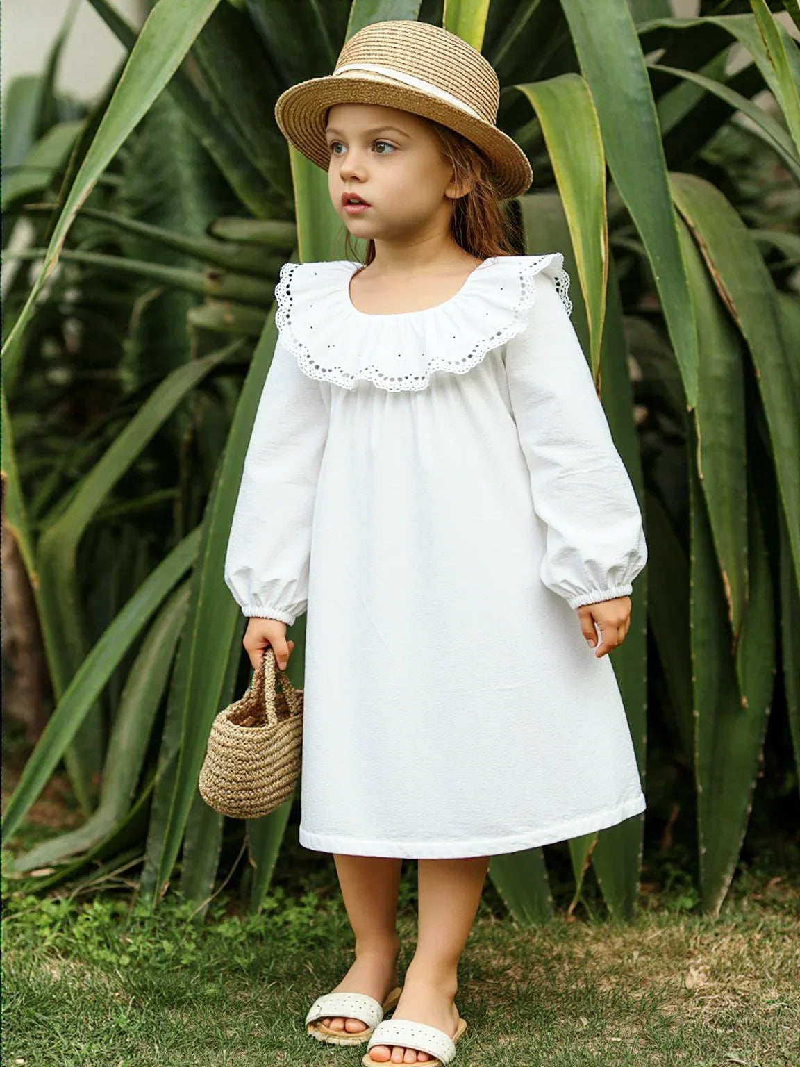 Young girl in a white dress and straw hat standing in front of green plants