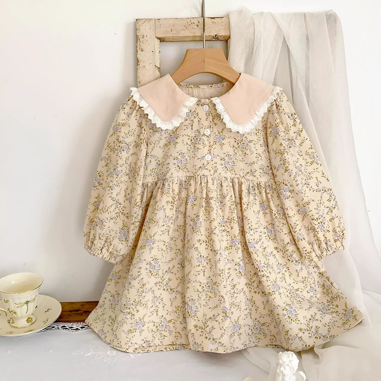 Floral dress with lace collar on a wooden hanger against a white wall.