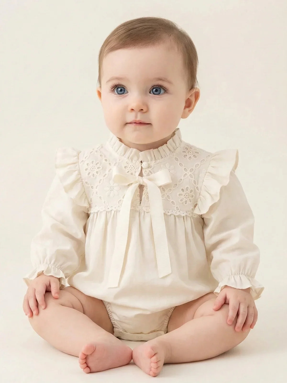 Baby's vintage antique white long sleeved romper set with lace accents on a beige background.