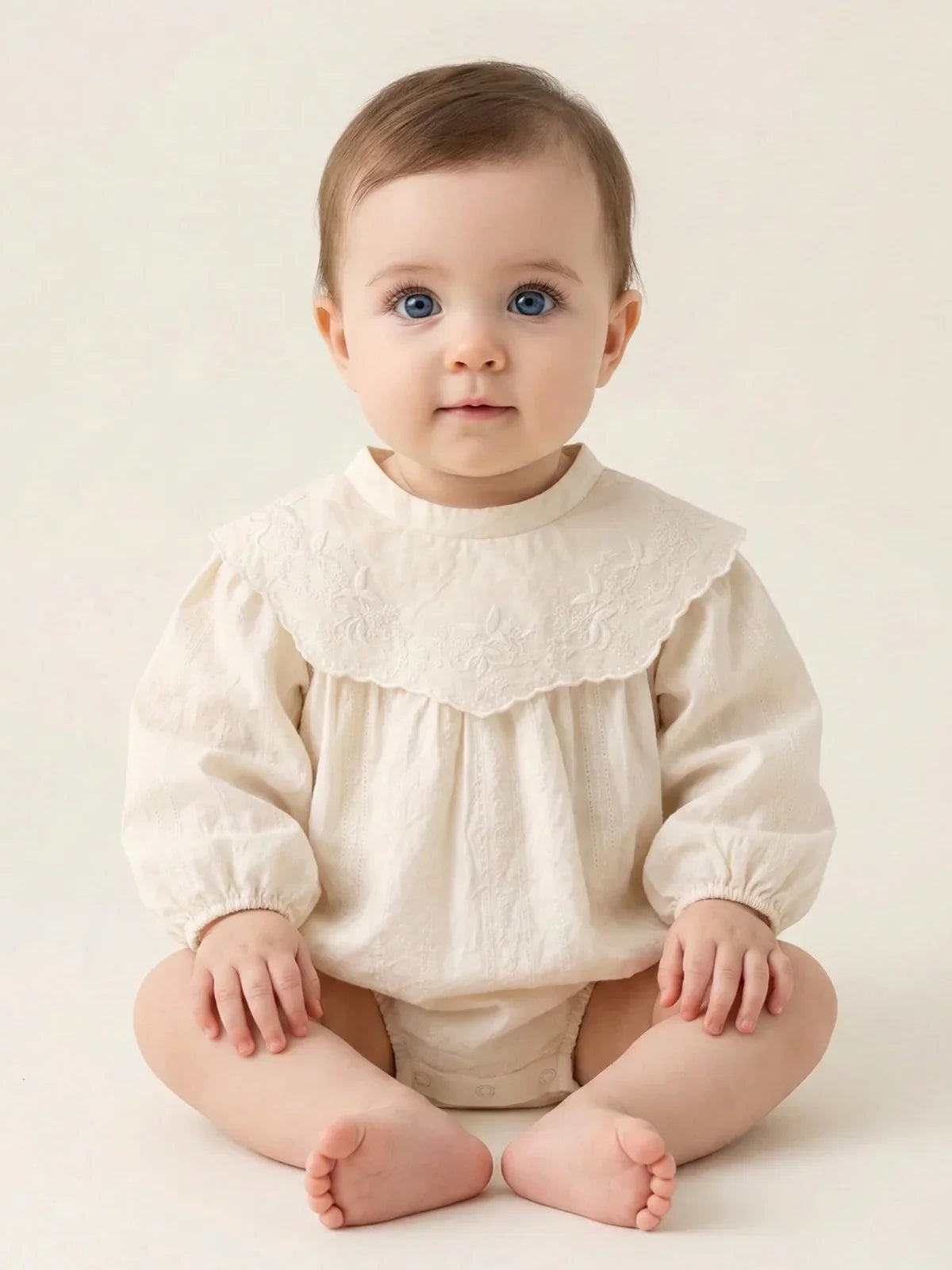 Baby wearing a vintage cream- colored long sleeved romper on a beige background.