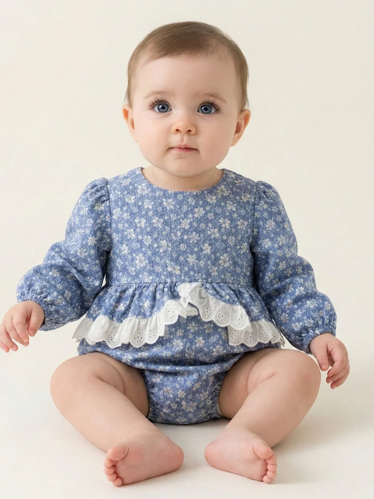 Baby wearing a blue floral romper with lace trim on a white background