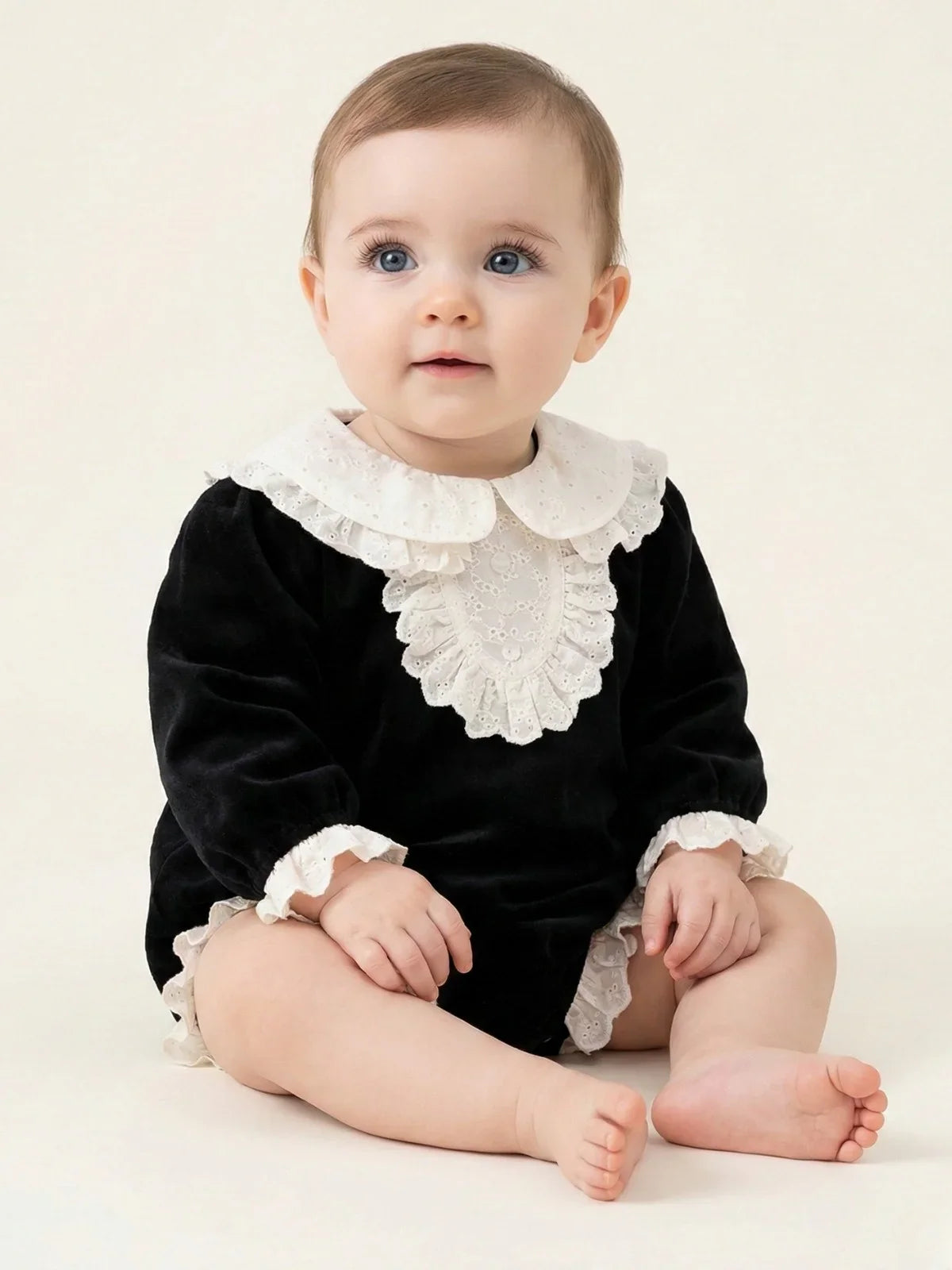 Baby wearing a black romper with white ruffled collar and cuffs on a light background