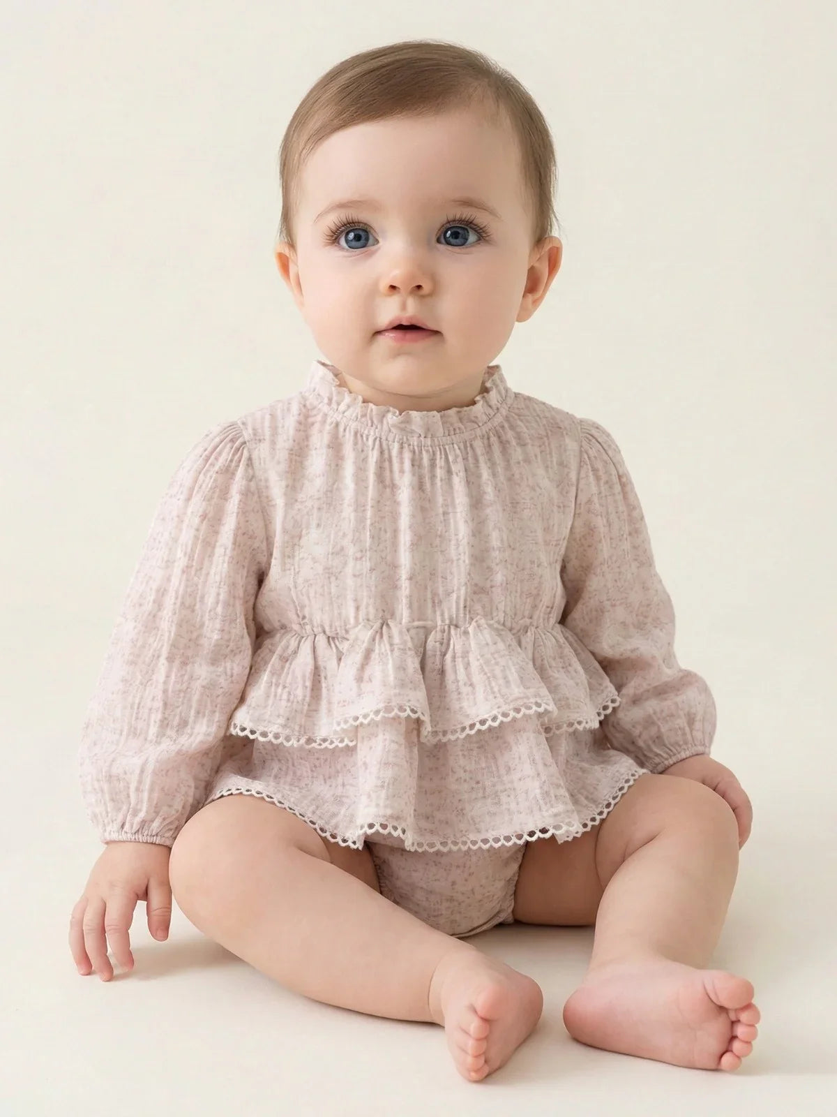 Baby wearing a pink romper with ruffled top and bloomers on a plain background