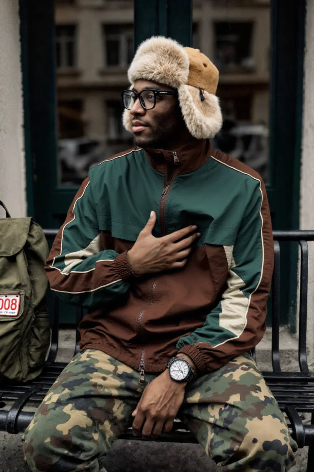 Person wearing a green and brown jacket with fur-lined hats, sitting on a bench.
