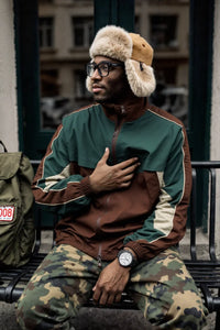 Thumbnail for Person wearing a green and brown jacket with fur-lined hats, sitting on a bench.