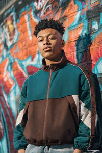 Thumbnail for Person wearing a green and brown jacket in front of a colorful graffiti wall