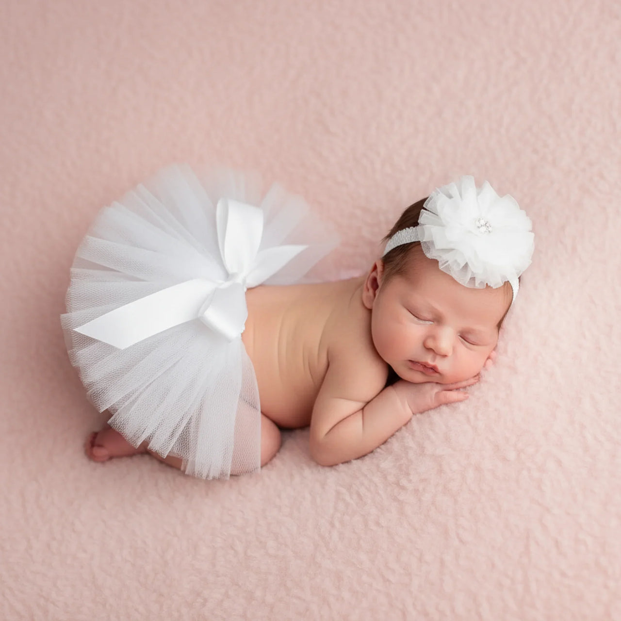 Newborn baby in a white tutu and headband on a pink background