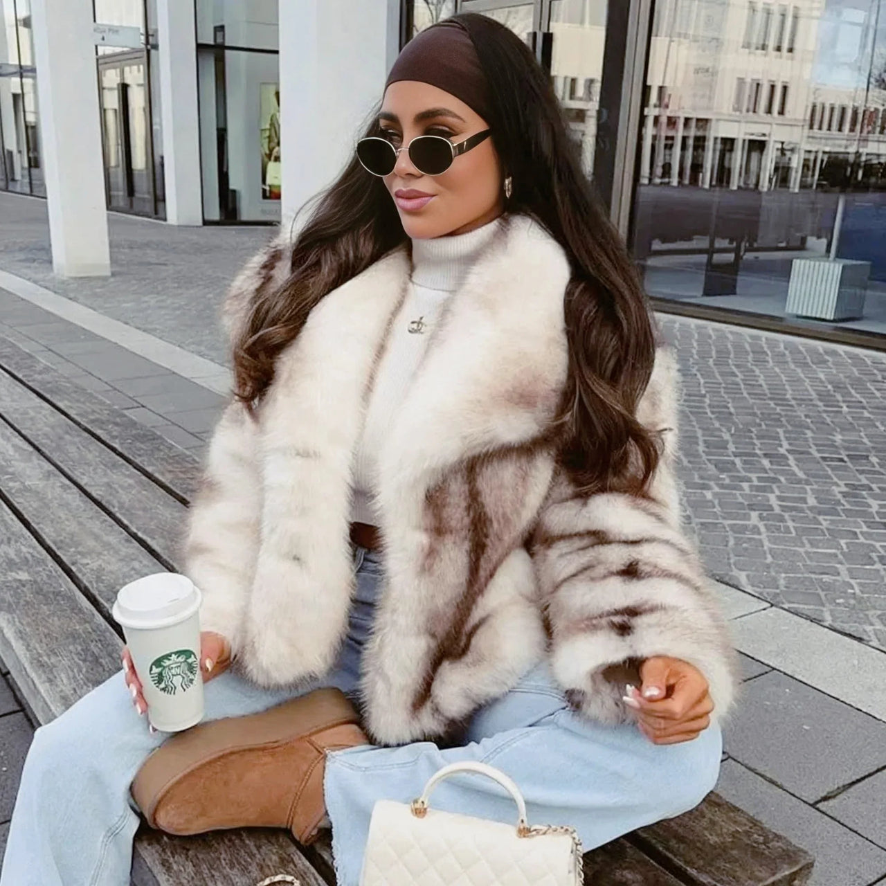 Woman in a white striped faux fur coat holding a Starbucks cup outdoors