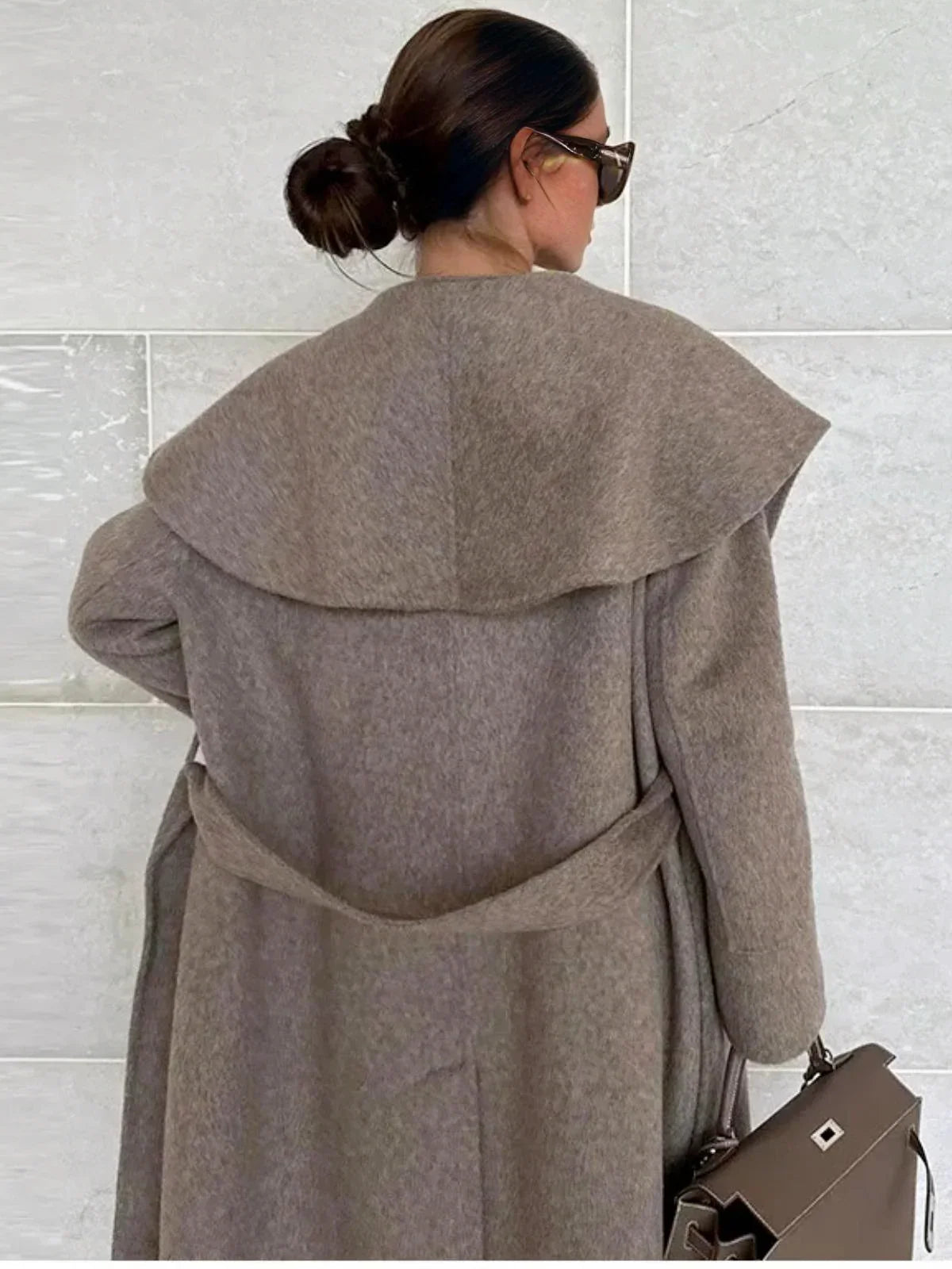 Back view of a woman wearing a long camel waterfall coat with belt and shawl lapel on a white background