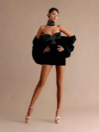 Thumbnail for Woman wearing a black mini dress with intricate detailing on a beige background