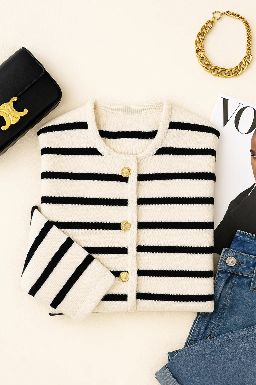 Women's black and white striped cardigan with gold buttons, black clutch, gold bracelet, and magazine on a white surface