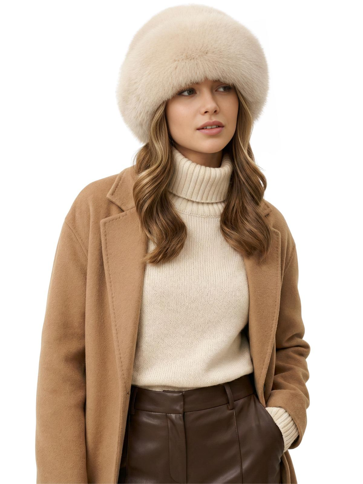 Woman wearing a beige faux fur hat, brown coat, white turtleneck sweater, and brown leather pants on a white background