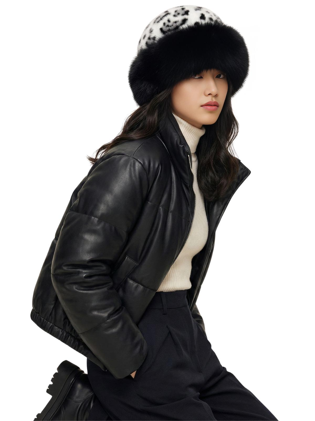 Person wearing a black leather jacket, white sweater, and dark pants with a white-black leopard print faux fur hat on a white background