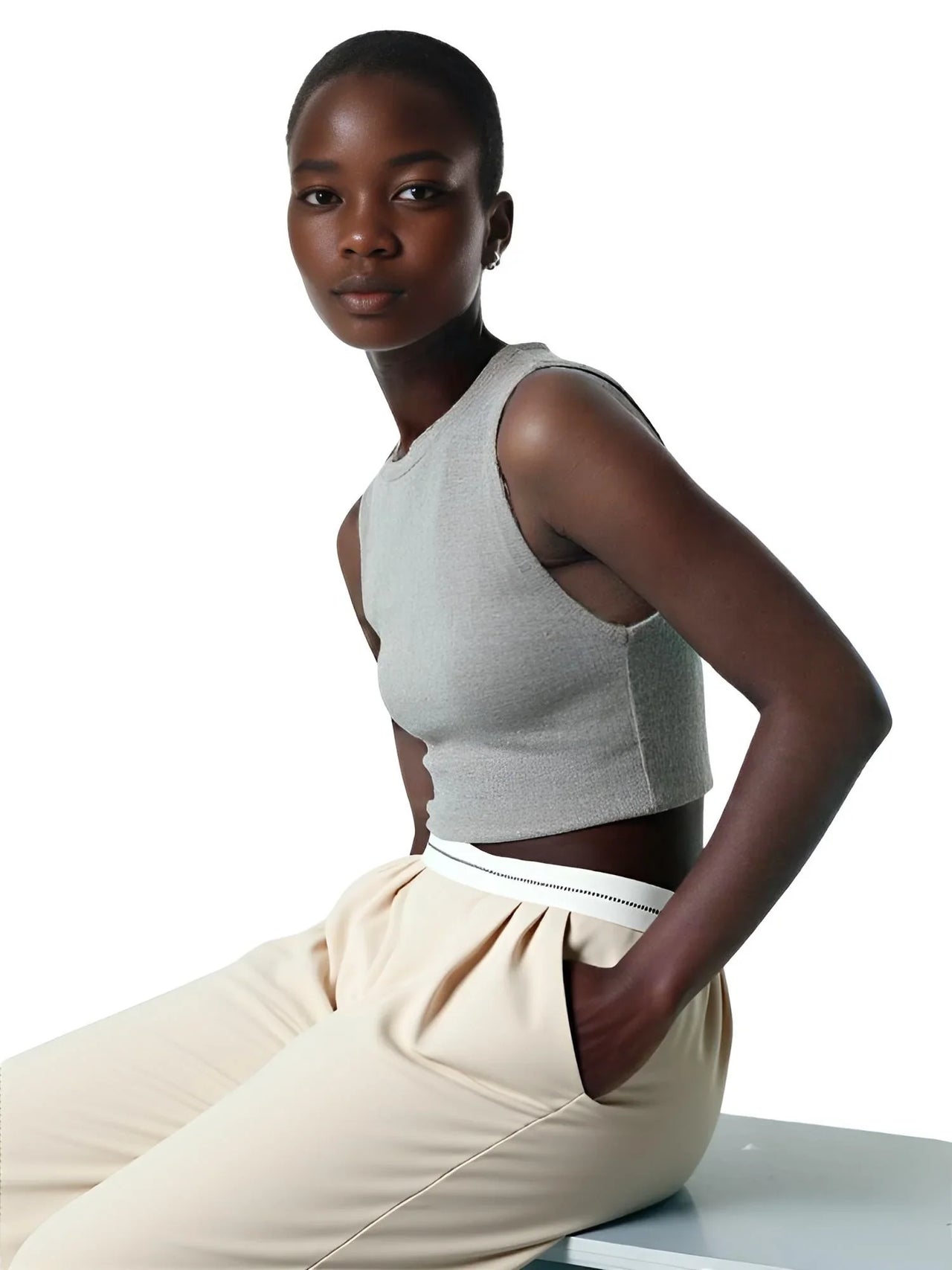 Woman wearing a gray sleeveless top and beige pants on a white background