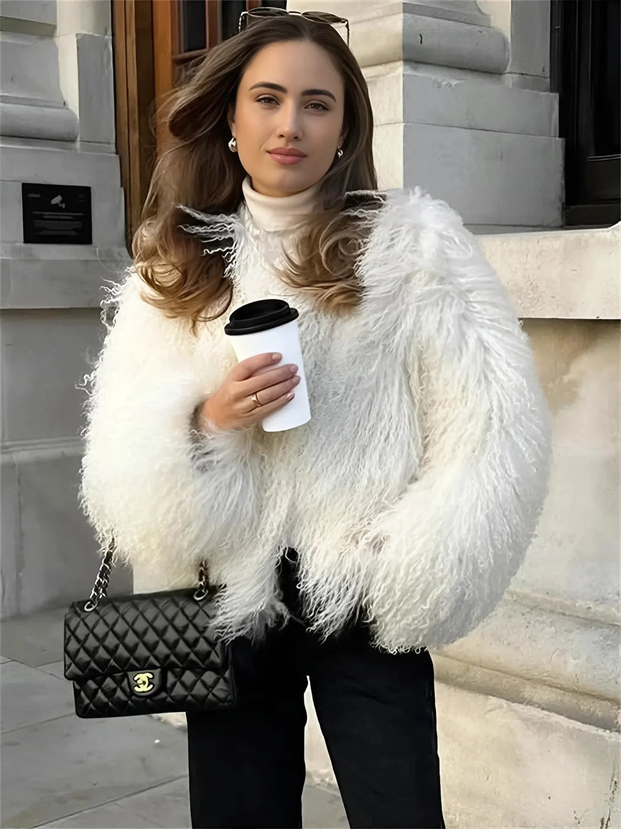 Woman in a white faux fur coat holding a coffee cup and a Chanel handbag.