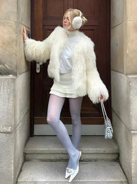 Thumbnail for Woman in a white outfit with faux fur coat and ear muffs standing on steps.