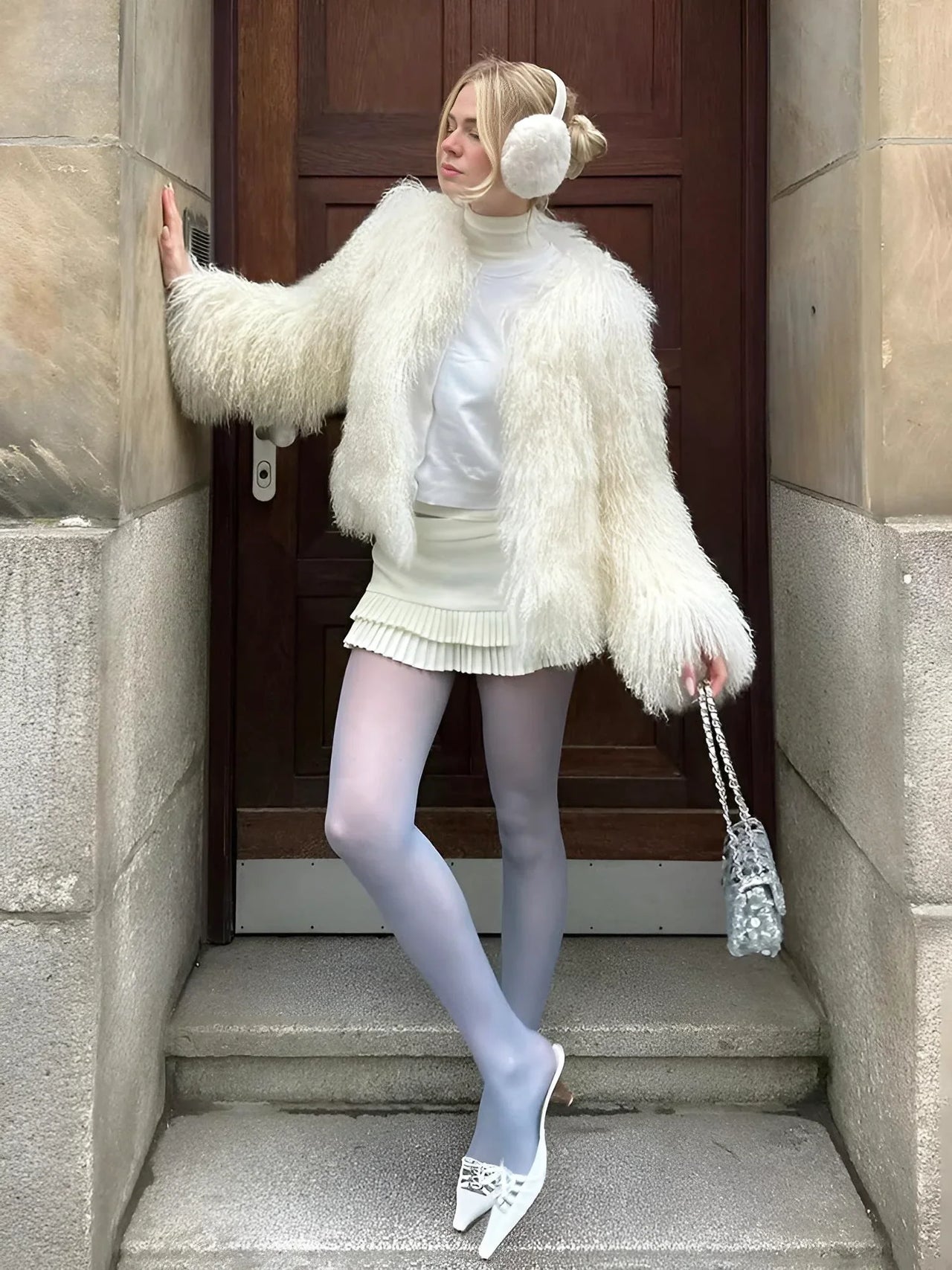 Woman in a white outfit with white faux fur coat and ear muffs standing on steps.