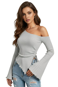 Thumbnail for Woman wearing an asymmetrical gray ribbed off-shoulder sweater with long flared sleeves and ripped jeans on a white background