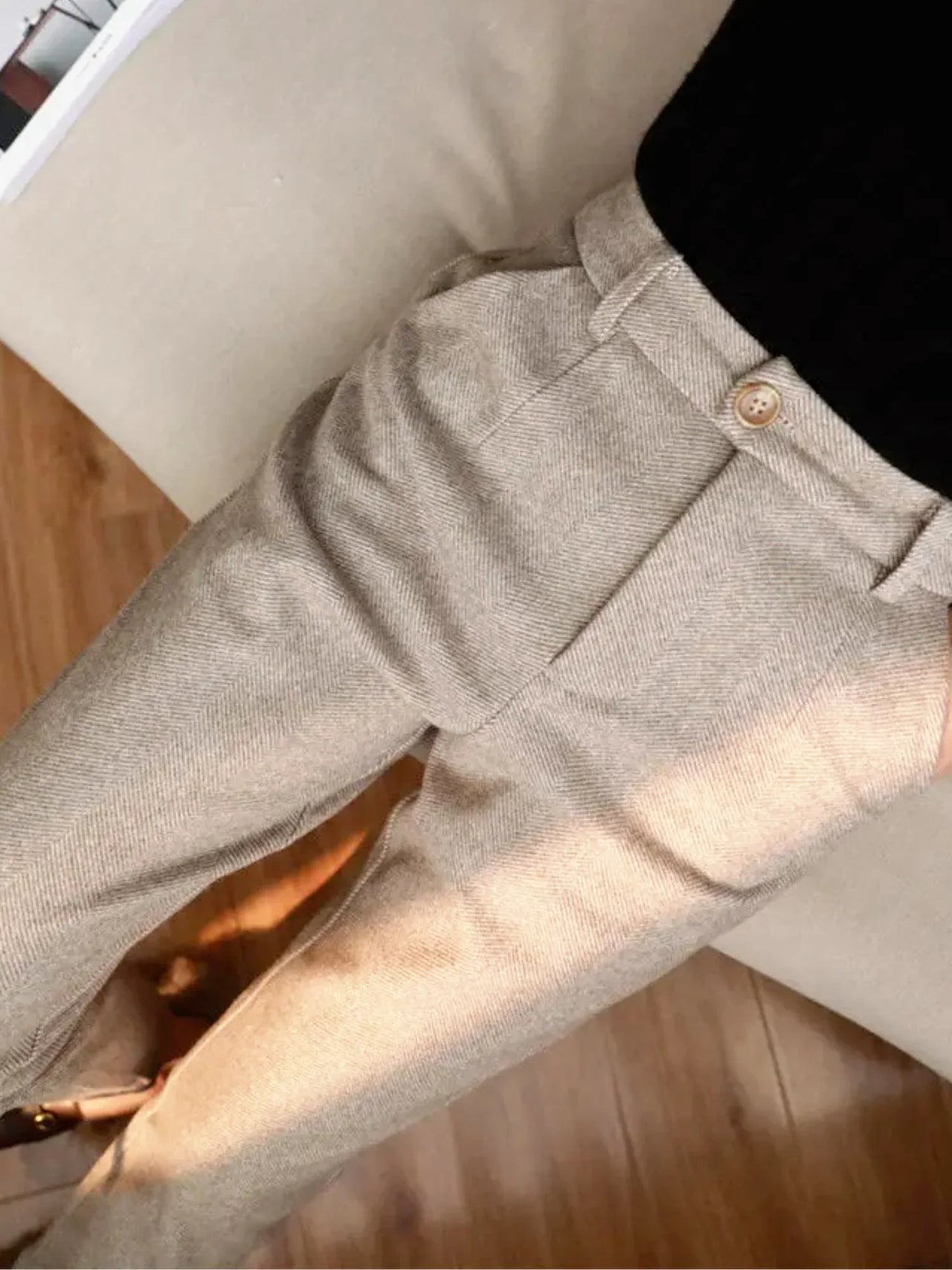Close-up of beige pants with a button on a wooden floor.