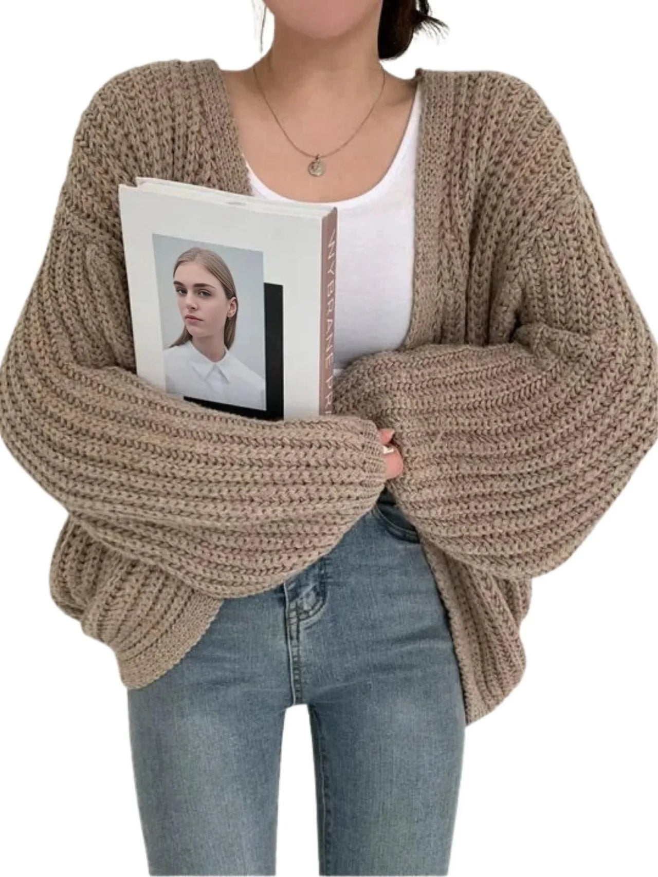 Person wearing a chunky knit cardigan holding a magazine with a white background