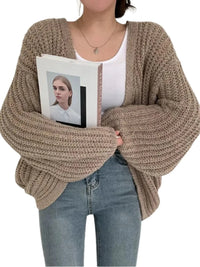Thumbnail for Person wearing a chunky knit cardigan holding a magazine with a white background